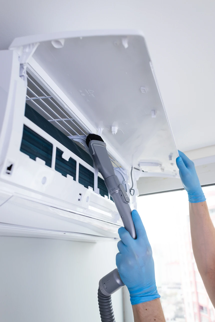 Intérieur résidentiel, technicien en gants bleus effectuant maintenance d'une unité de climatisation murale