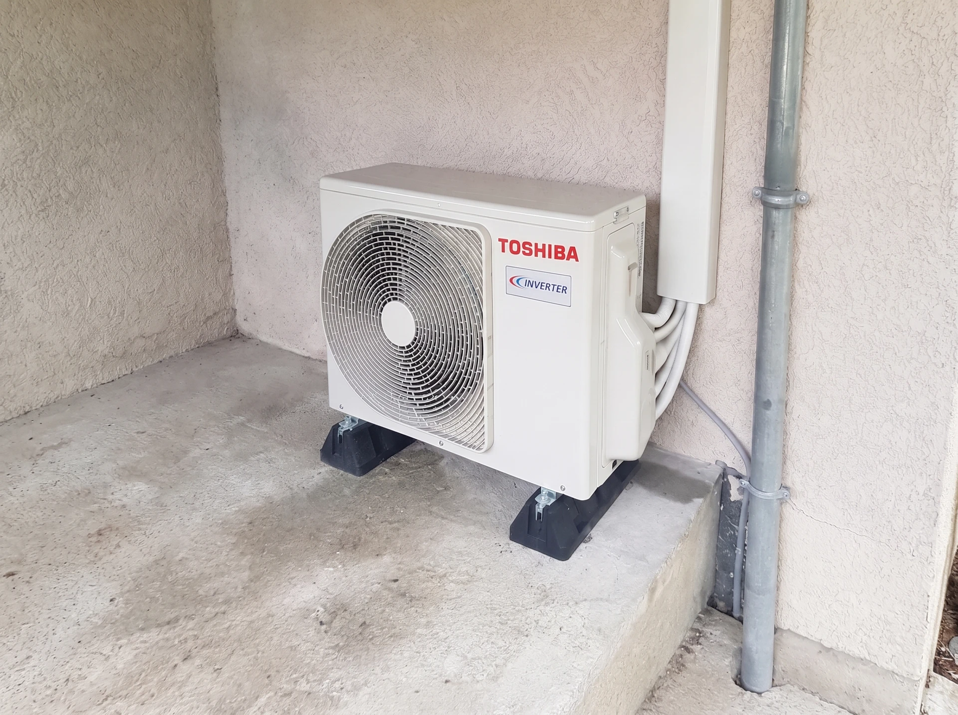 Installateur en combinaison beige travaille sur système de plancher chauffant hydraulique, connectant tuyaux PEX au collecteur-répartiteur avec vannes rouges et bleues